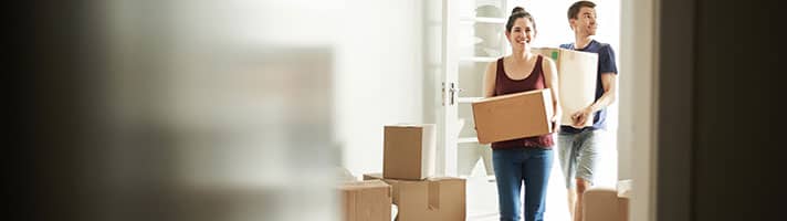 Man and woman entering house holding boxe.