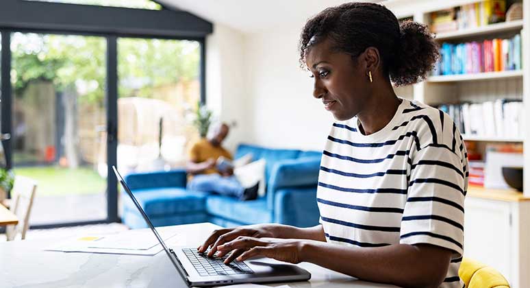 Woman with stripy t-shirt on laptop at the kitchen table.