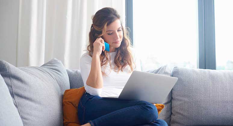 Woman on a sofa with laptop and phone.