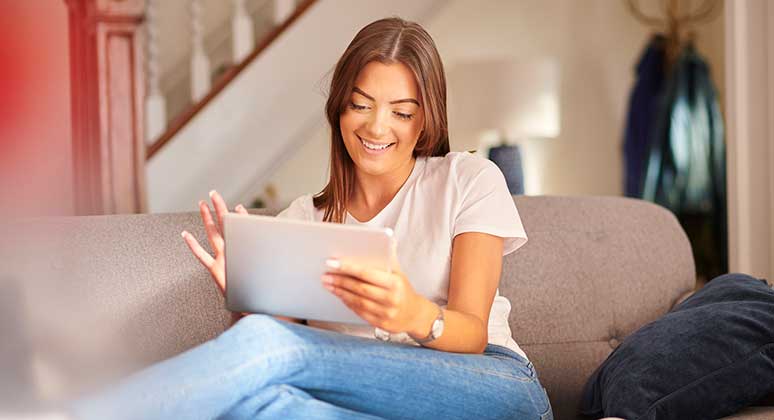 Woman sat on a sofa with a tablet device.